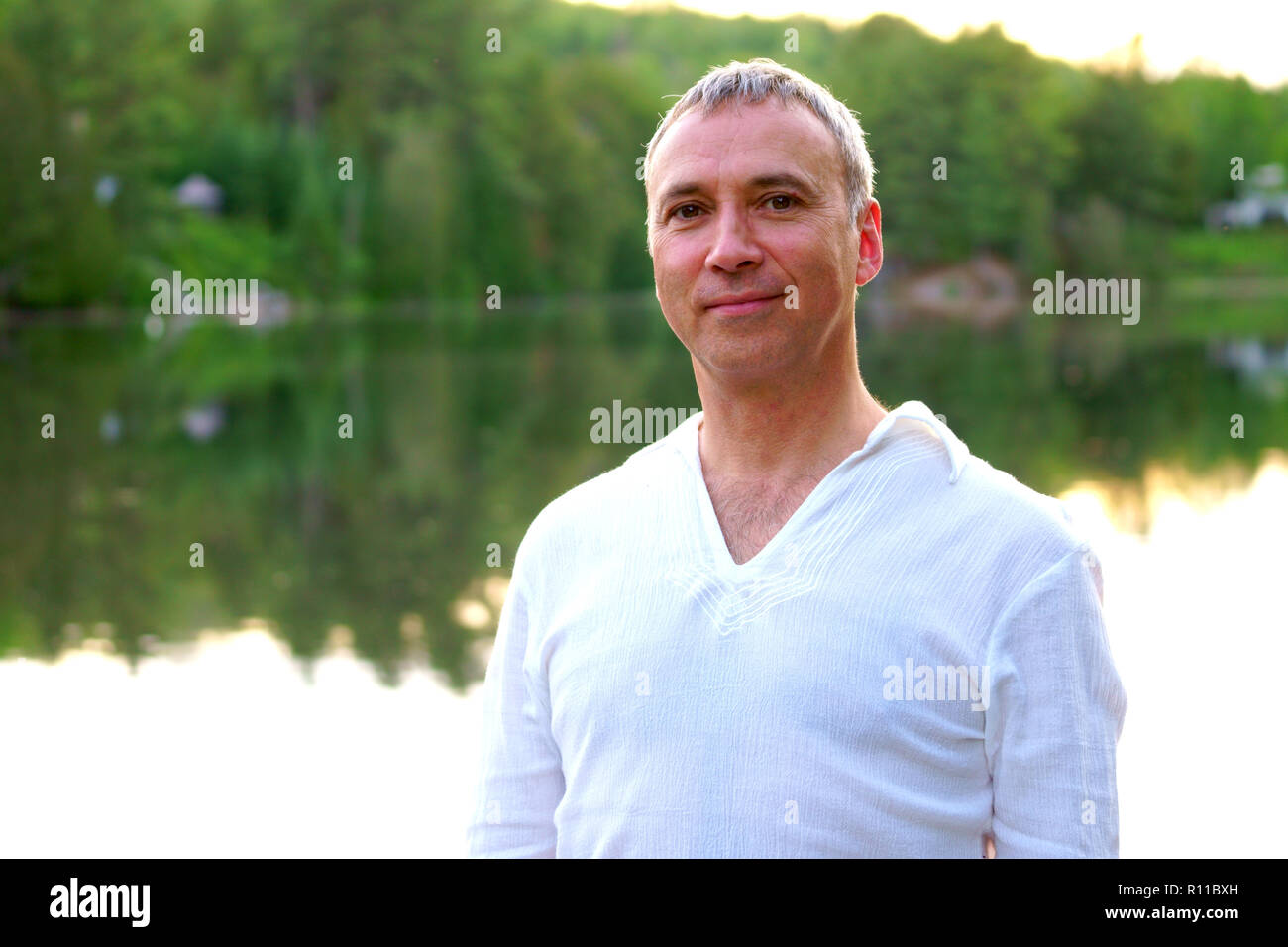 Portrait d'une saine fierté caucasian man, 50 ans, vêtu d'un costume blanc, après une session de méditation par la rivière au coucher du soleil. Banque D'Images