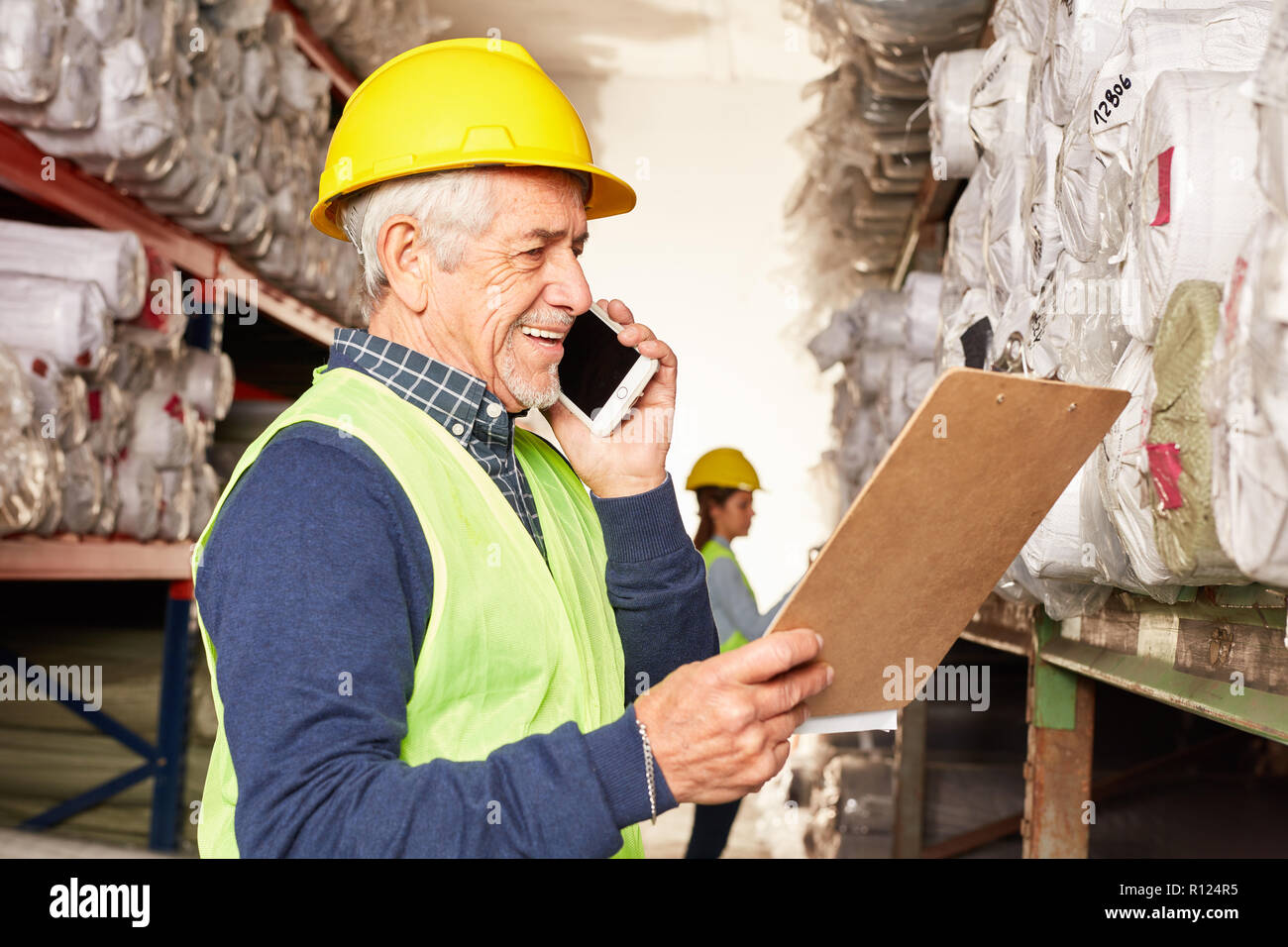 Employé de l'entrepôt est heureux à propos d'un message sur le smartphone dans l'entrepôt de tapis Banque D'Images