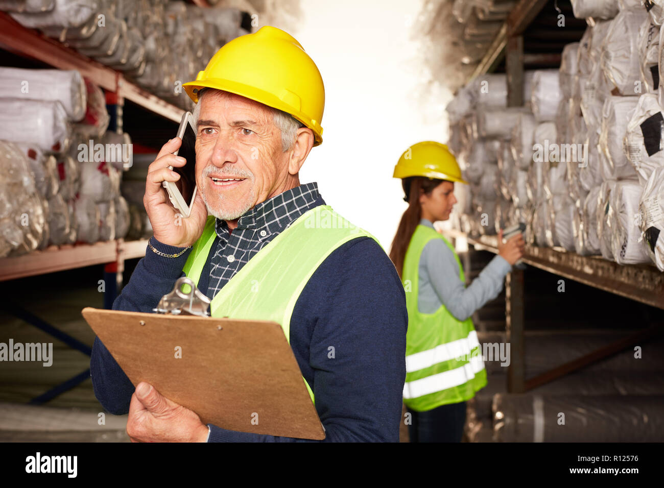 Ancien travailleur de la logistique est de téléphoner avec le smartphone dans l'entrepôt de tapis Banque D'Images