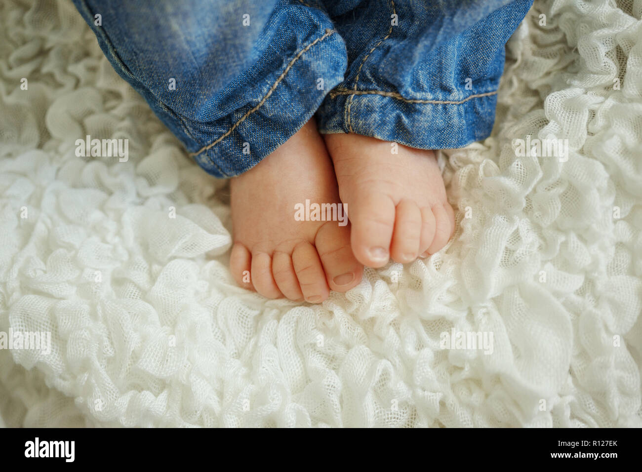 Les jambes à la mode nouveau-né. Petit enfant en jeans dormir à couverture blanche, allongé sur le lit. Banque D'Images