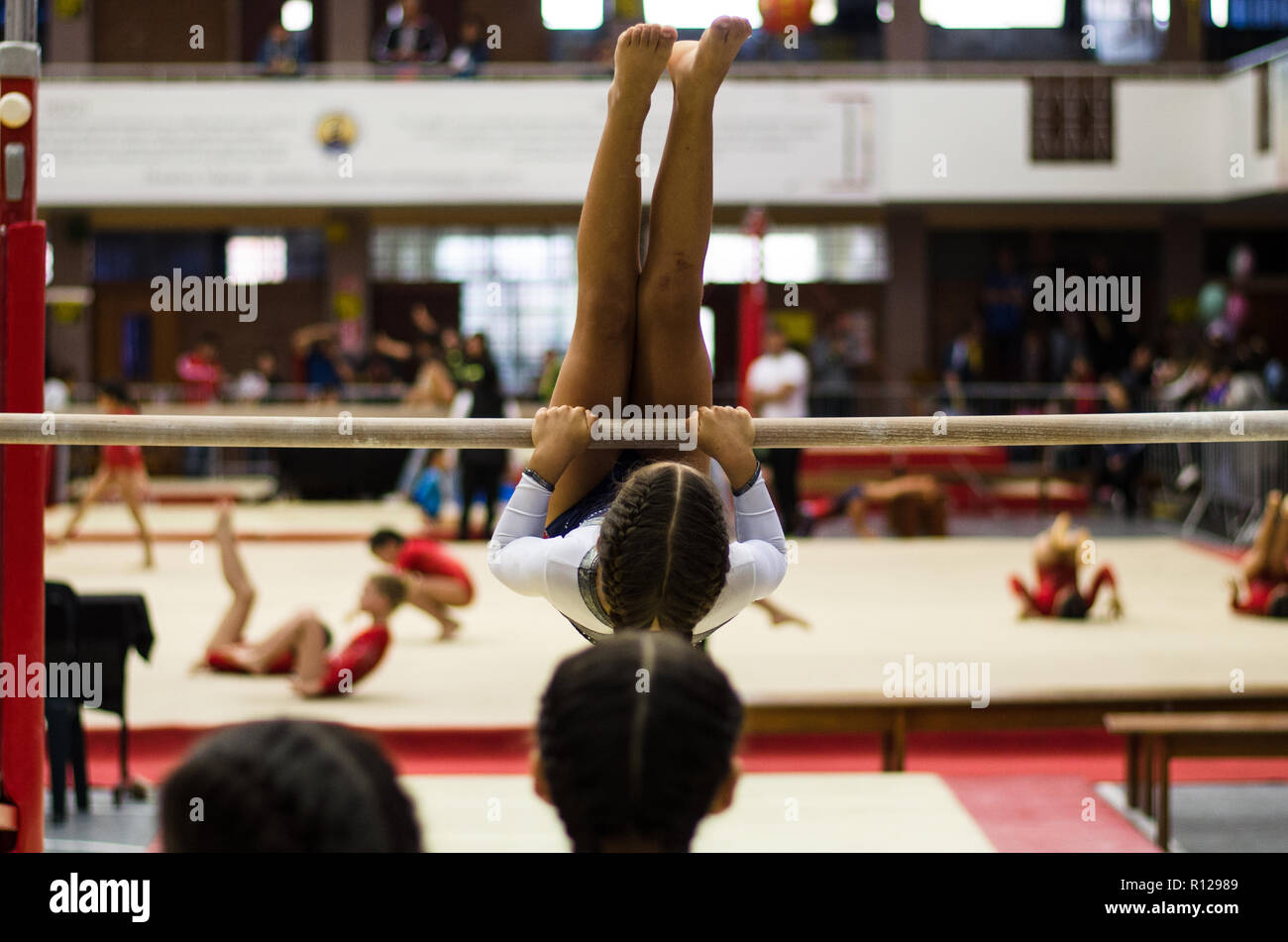 Petite fille athlétique gymnaste exécutant les exercices au bar dans le championnat Banque D'Images