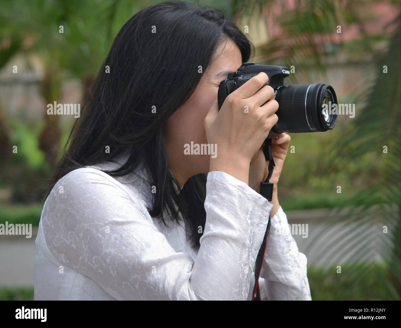 Jeune femme photographe vietnamien porte une robe traditionnelle blanche et est titulaire d'un appareil photo reflex numérique Canon avec les deux mains. Banque D'Images