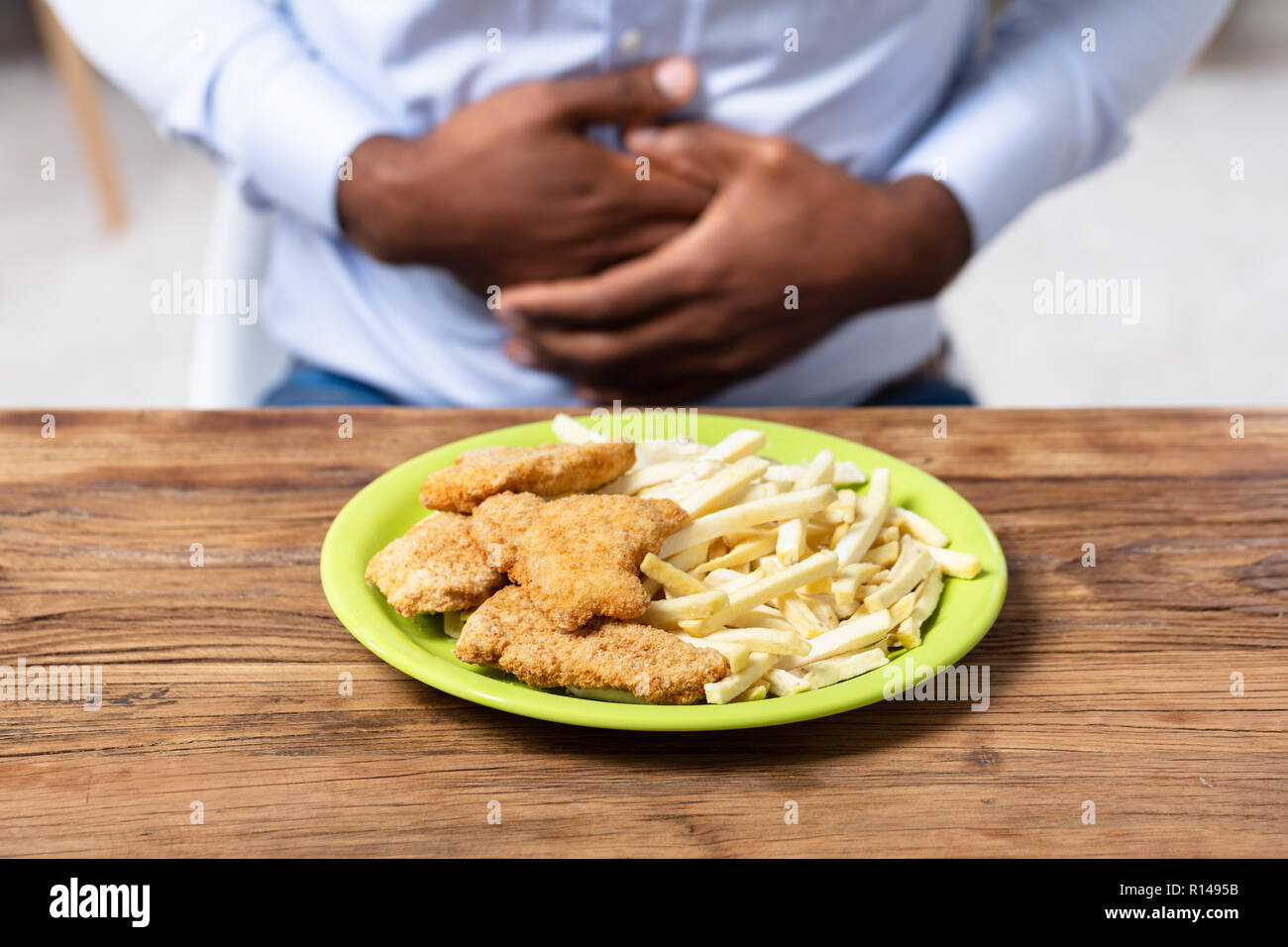 Les aliments frits sur la plaque en face de l'homme ayant des douleurs à l'estomac Banque D'Images