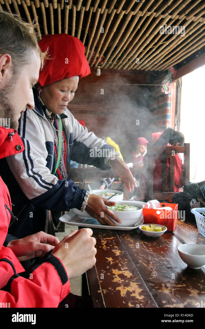 Femme dzao rouge sert ga pho (soupe au poulet et nouilles) à un touriste allemand à son village eatery près de Sapa, Vietnam Banque D'Images