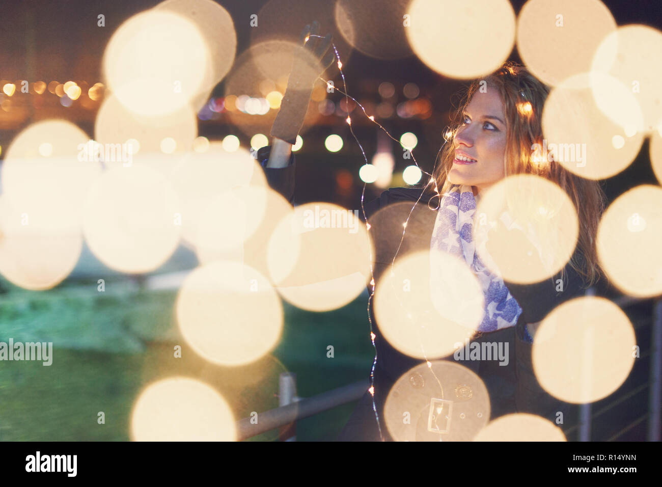 Jeune femme jouant avec fairy lights au winter outdoor looking away Banque D'Images