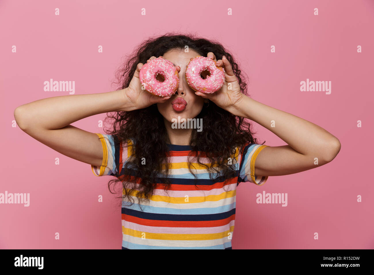Photo de femme drôle 20s avec des cheveux bouclés le bouffon et holding donuts plus isolé sur fond rose Banque D'Images