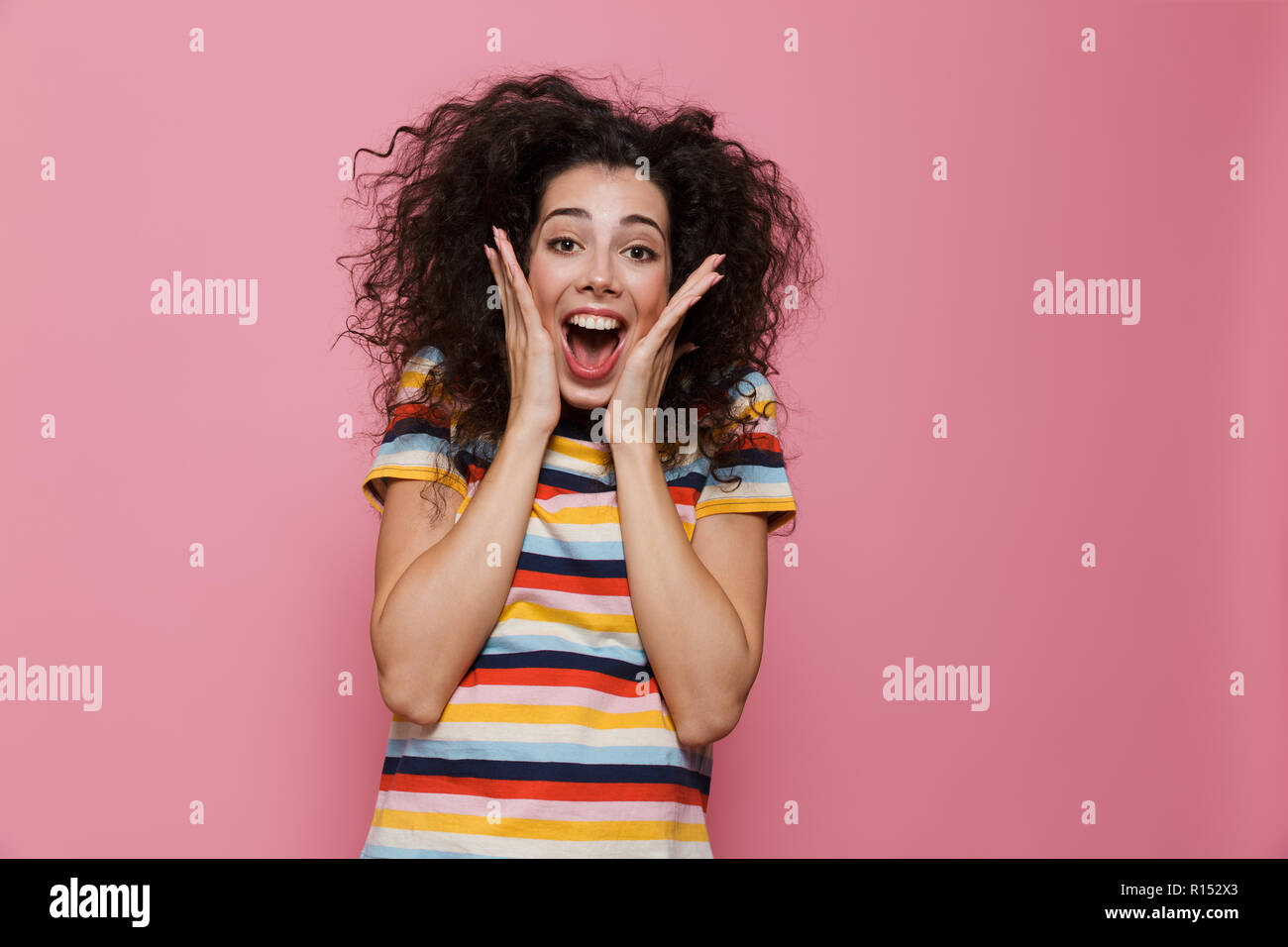 Image femme 20s avec les cheveux bouclés et visage souriant toucher isolés sur fond rose Banque D'Images