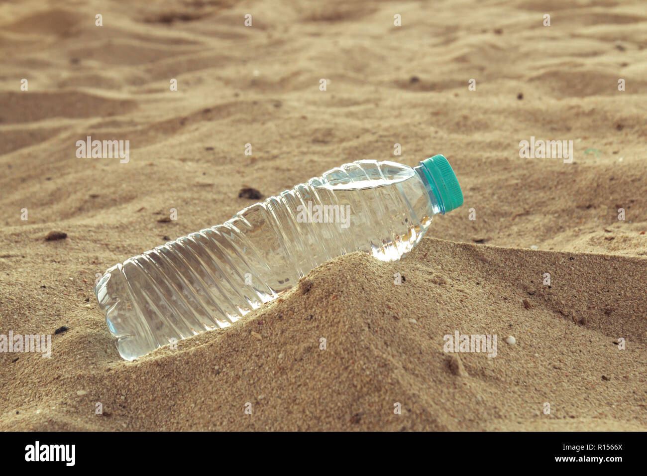Bouteille PET avec de l'eau sur le désert. Une bouteille d'eau se trouvant dans le sable chaud du désert. Banque D'Images