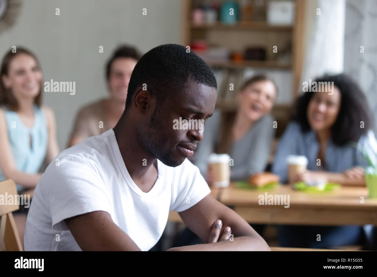 Divers Groupe de gens assis dans un café en riant la moquerie à l'homme noir. L'accent sur assis séparément l'homme sent en colère et malheureux, camarades de ne pas le prendre Banque D'Images