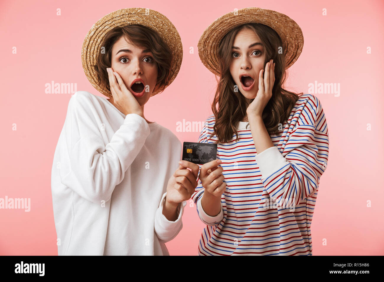 Image de jolies jeunes femmes excitées choqué friends posing isolé sur fond rose holding credit card. Banque D'Images