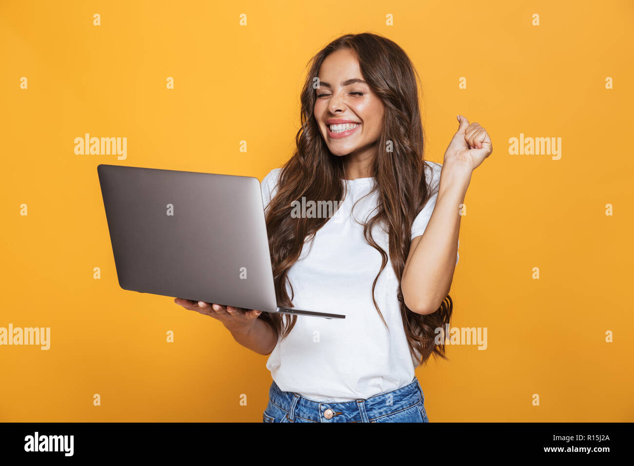 Portrait de femme brune 20s avec de longs cheveux gris et en joie ordinateur portable isolé sur fond jaune Banque D'Images