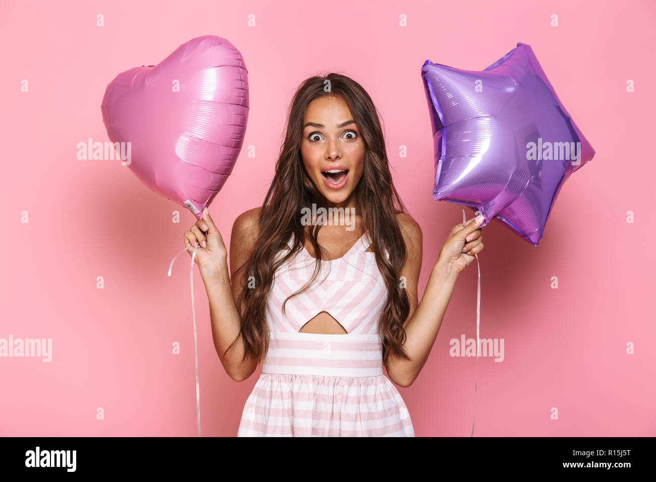 Portrait de jeune fille brune 20s aux cheveux longs portant de robe deux ballons plus isolé sur fond rose Banque D'Images