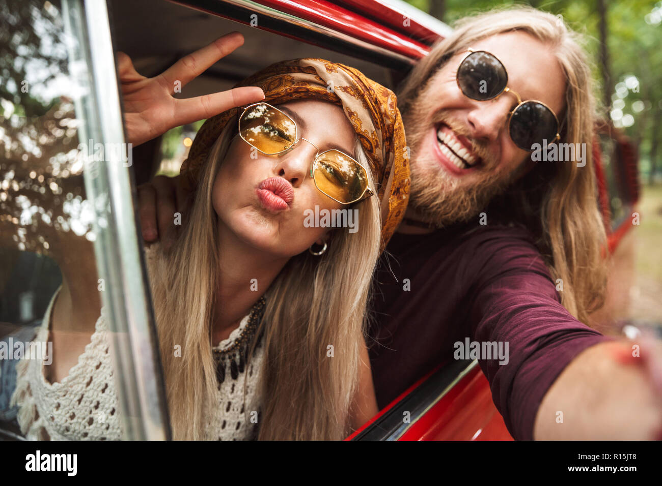 Photo de type couple hippie montrant signe de paix en conduisant une fourgonnette rétro en forêt Banque D'Images