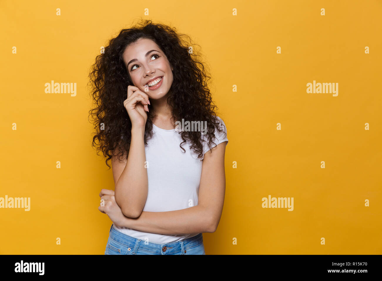 Image de gorgeous woman 20s avec les cheveux bouclés et souriant à la recherche sur fond jaune isolé vers le haut Banque D'Images
