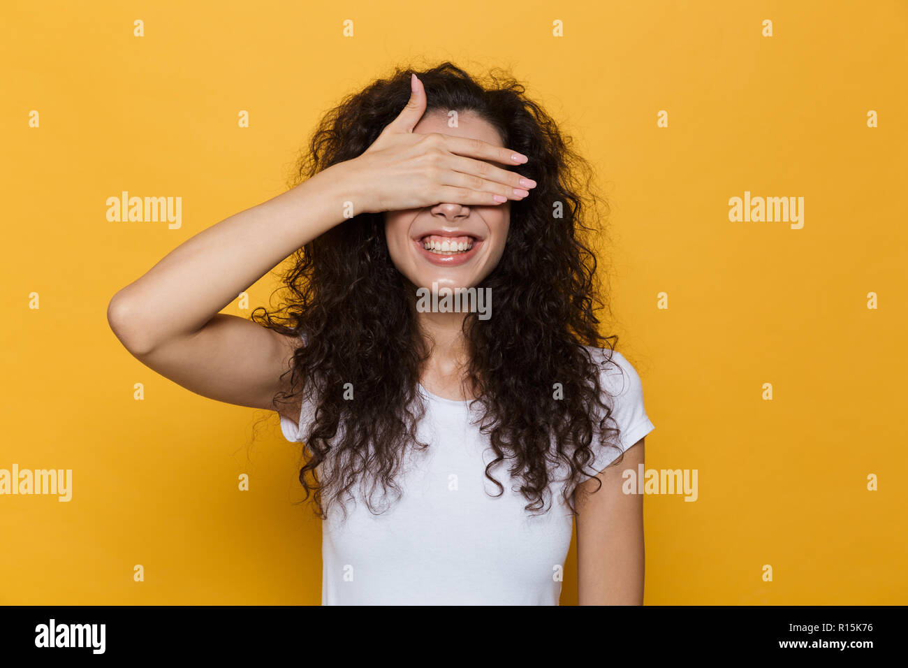 Image de femme brune 20s avec les cheveux bouclés de sourire et les yeux avec revêtement isolé sur fond jaune palm Banque D'Images