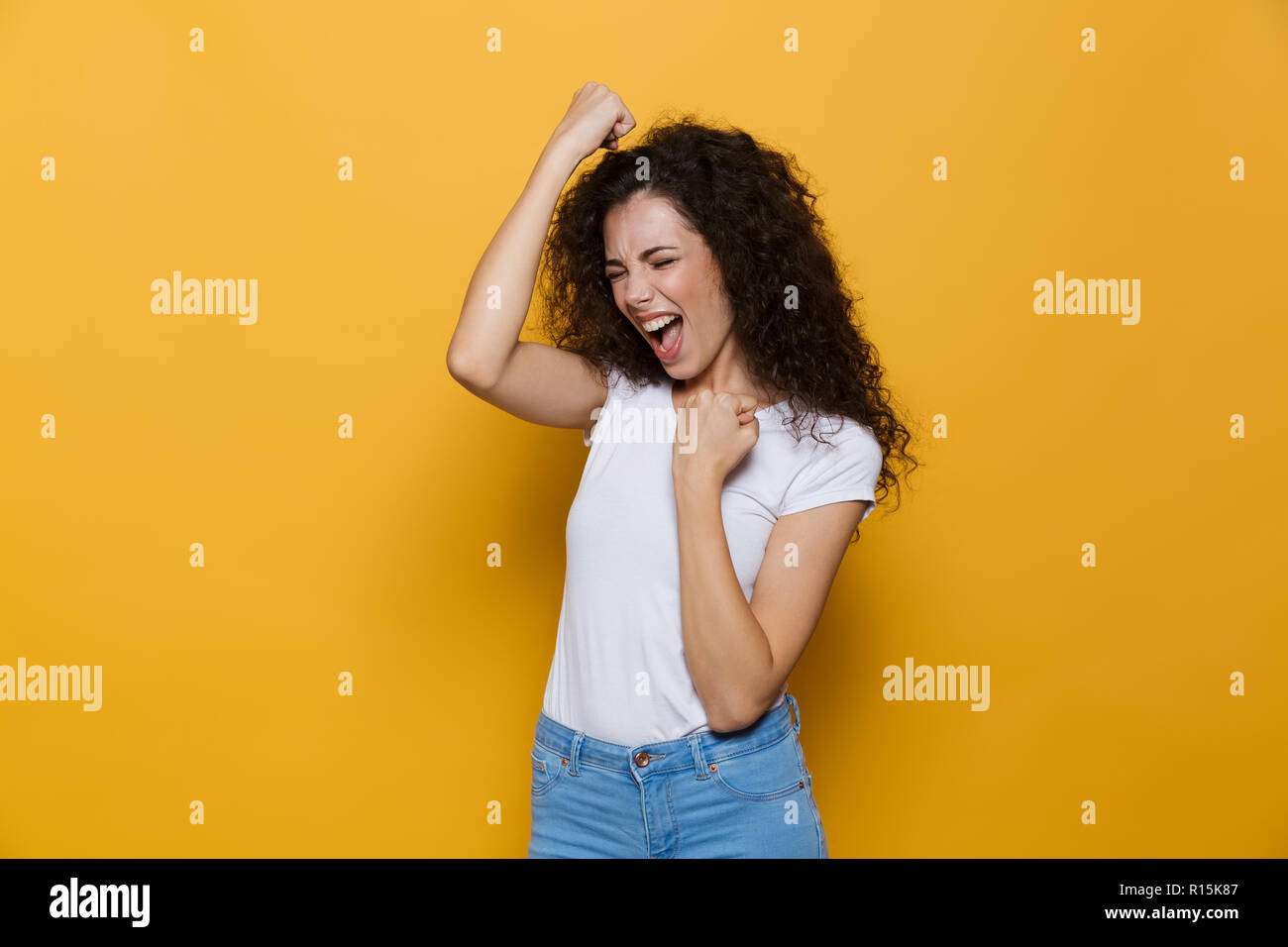 Image de femme joyeuse 20s avec les cheveux bouclés en criant et isolé pebbles sur fond jaune Banque D'Images