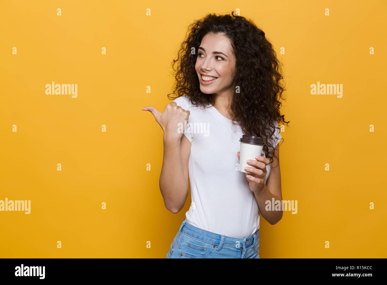 Image de femme brune 20s avec des cheveux bouclés beach café à emporter dans la tasse de papier sur fond jaune isolé Banque D'Images