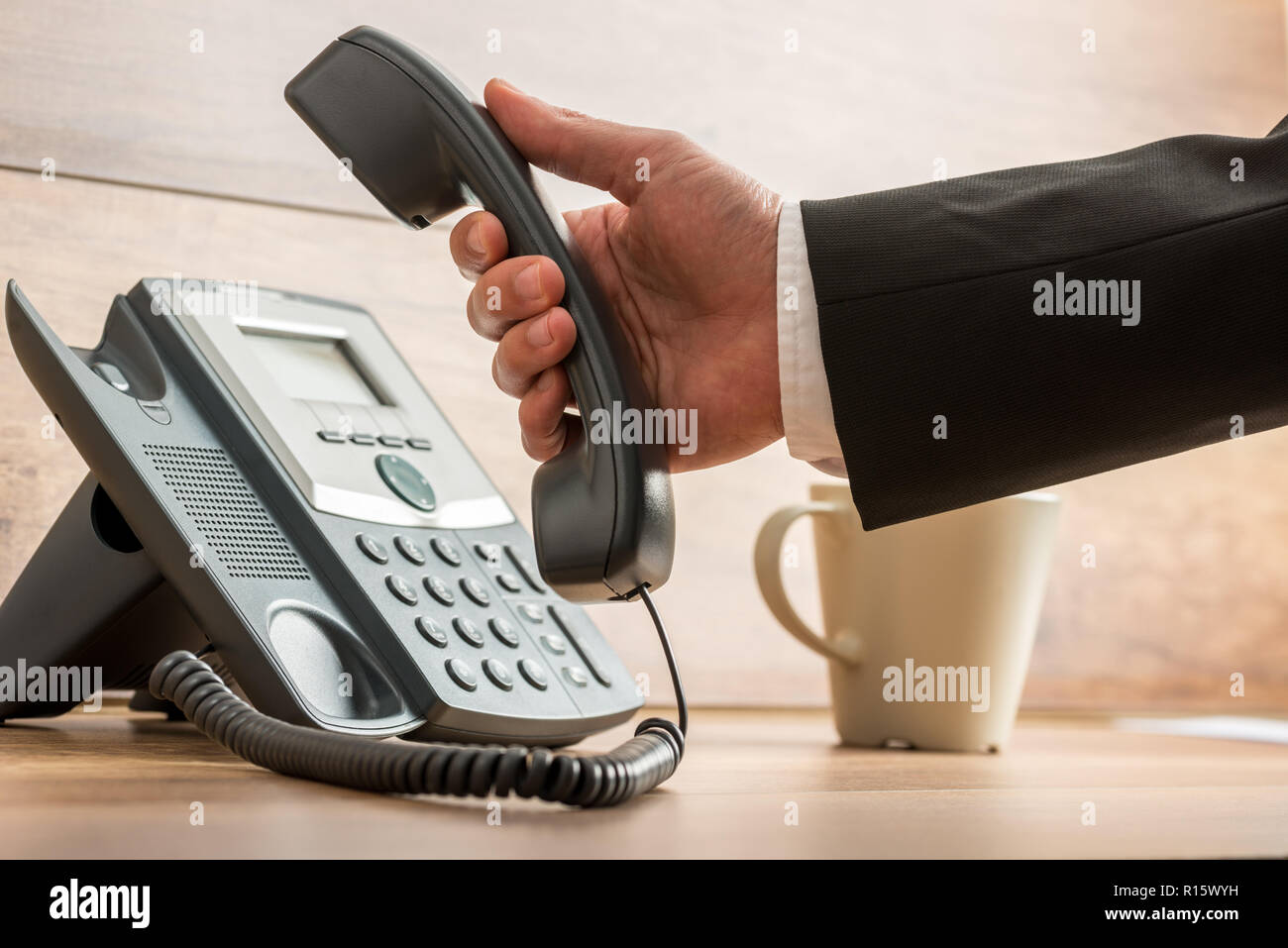 Gros plan du businessman hanging ou en décrochant un téléphone fixe combiné sur meubles de bureau en bureau avec une tasse de café à côté. Banque D'Images