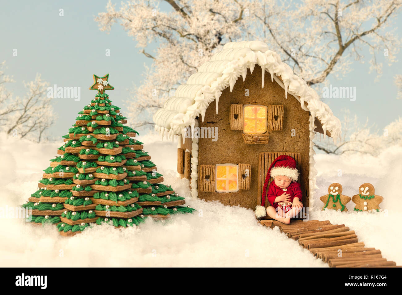 Image composite d'un nouveau-né en face d'une maison en pain d'épices de Noël dans un paysage de neige Banque D'Images
