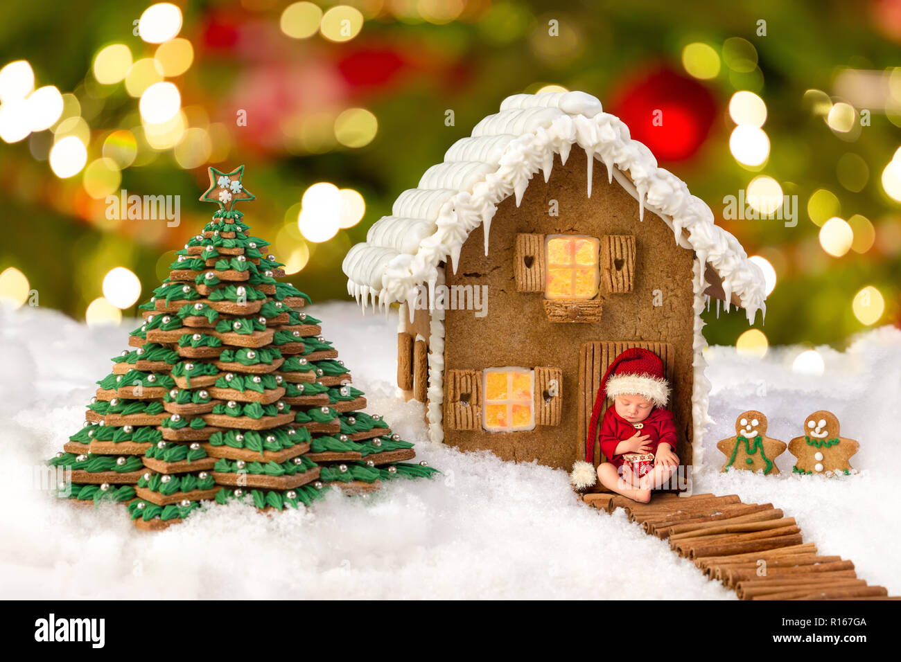 Image composite d'un nouveau-né en face d'une maison en pain d'épices de Noël dans un paysage de neige Banque D'Images