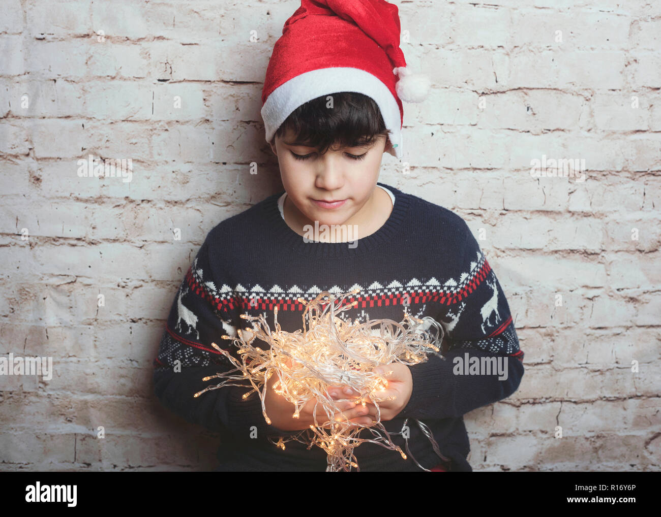 Enfant avec des lumières de Noël sur fond brique Banque D'Images