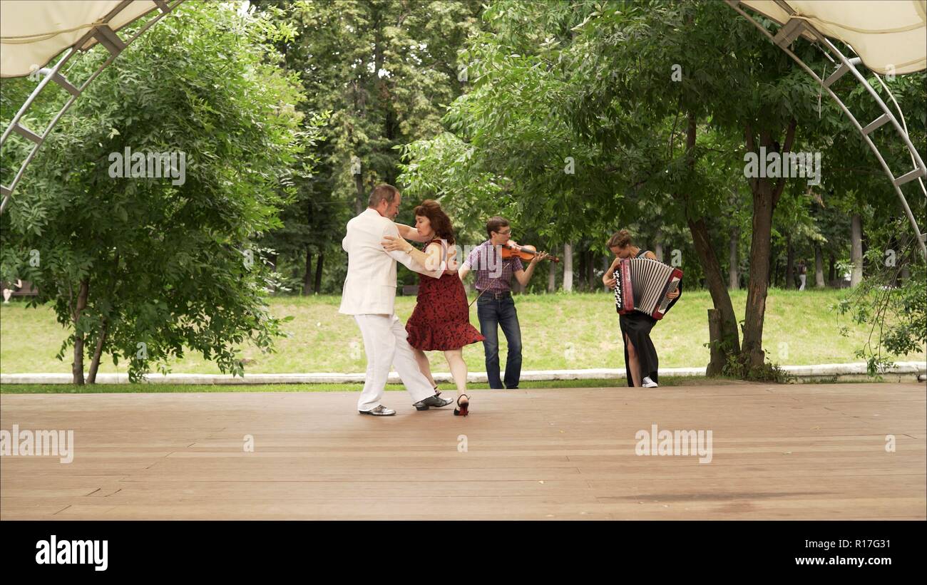 Accordéon et violon jouant dans le parc. Une femme dans une robe rouge et un homme dans un costume blanc sont la danse tango. Un couple de personnes âgées danser le tango dans le parc. Banque D'Images