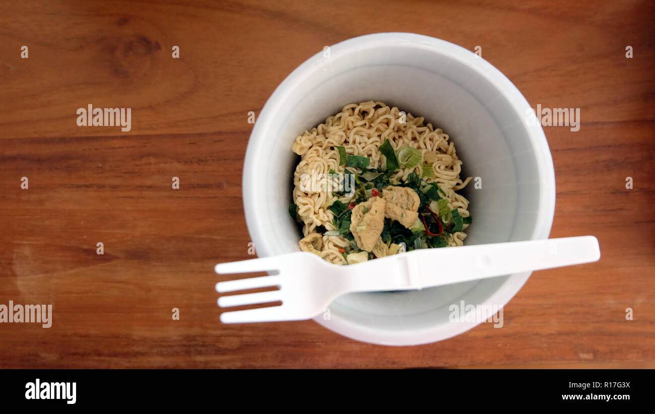 Vue de dessus d'un instant cup noodle, sans eau et couvercle, sur une table en bois. Les nouilles sèches peut être vu à l'intérieur. Une fourchette en plastique est placé sur le haut. Banque D'Images