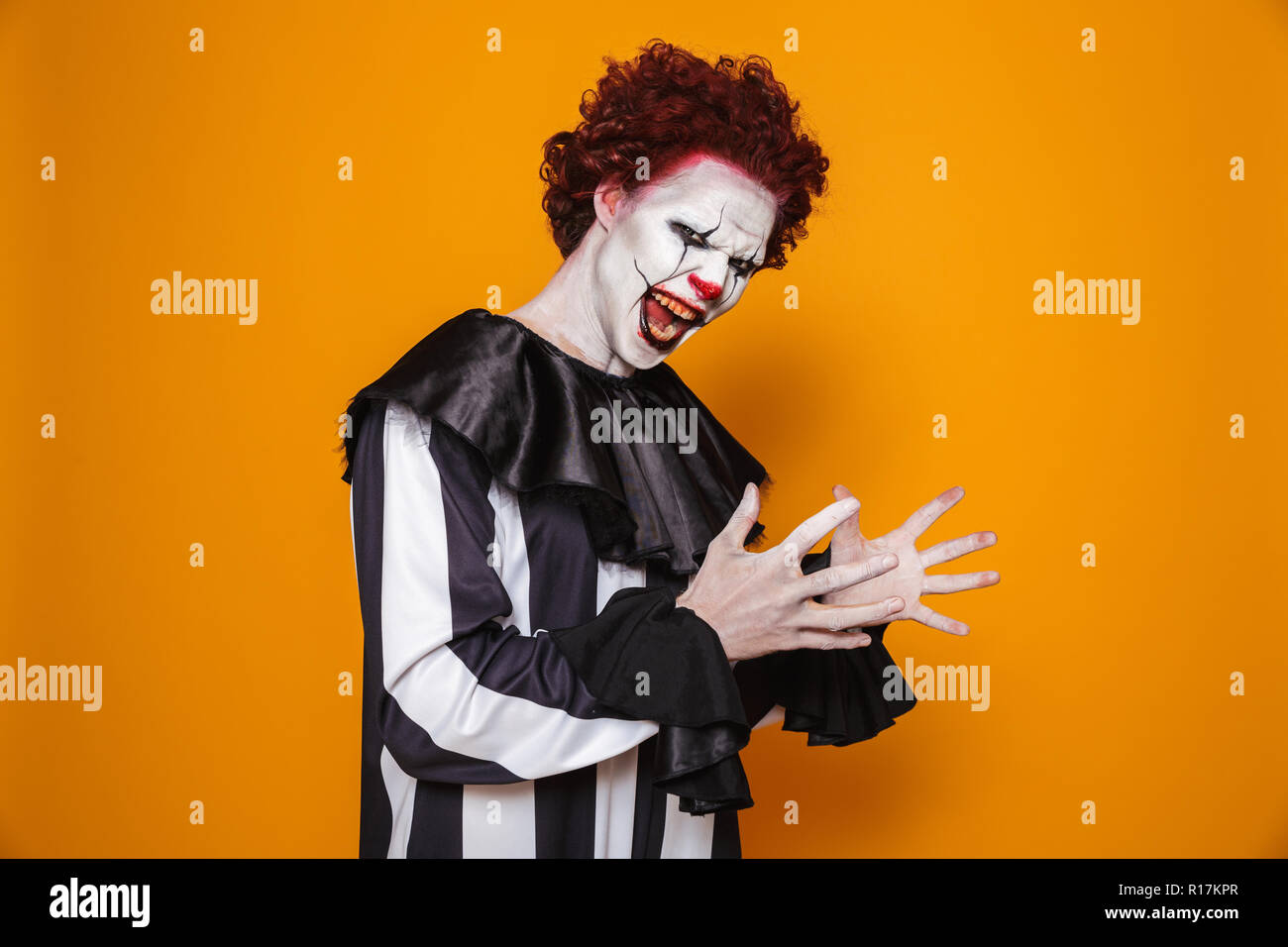 Scary clown en colère l'homme aux cheveux rouges à la caméra et crier sur orange isolé Banque D'Images