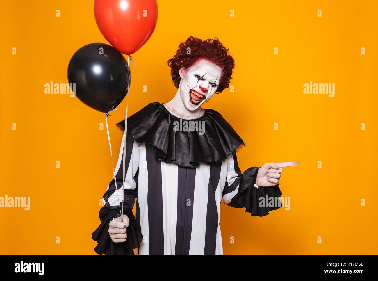 Homme en colère habillé en clown effrayant Halloween Costume holding  balloons isolé sur fond jaune Photo Stock - Alamy