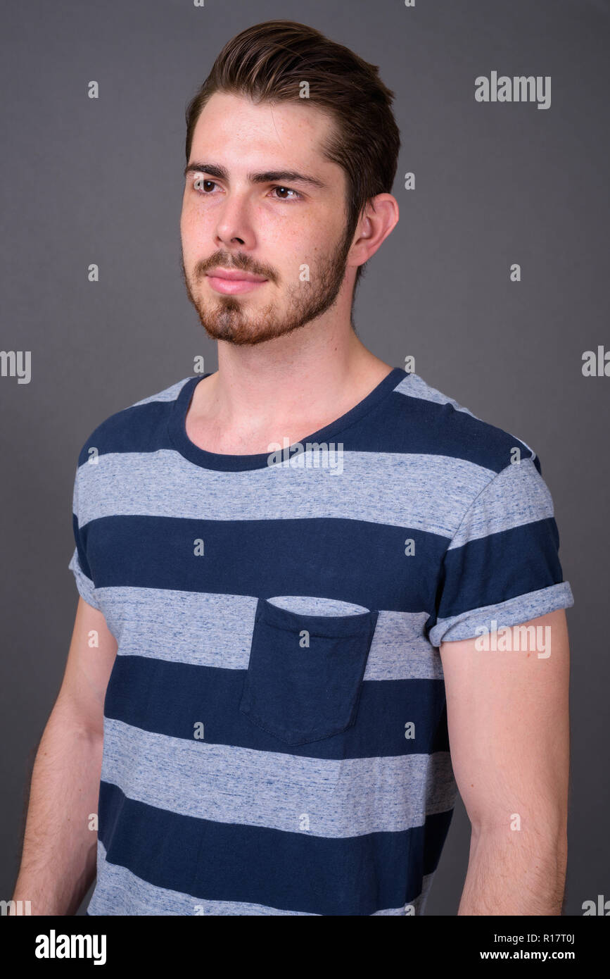 Beau jeune homme barbu contre l'arrière-plan gris Banque D'Images