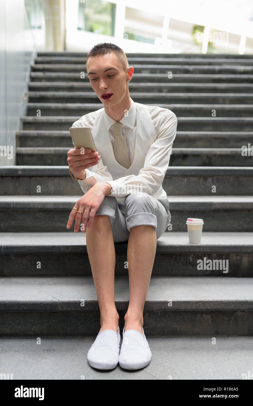 Les jeunes LGBT homosexuel androgyne businessman sitting on stairs lors de l'utilisation de Phone Banque D'Images