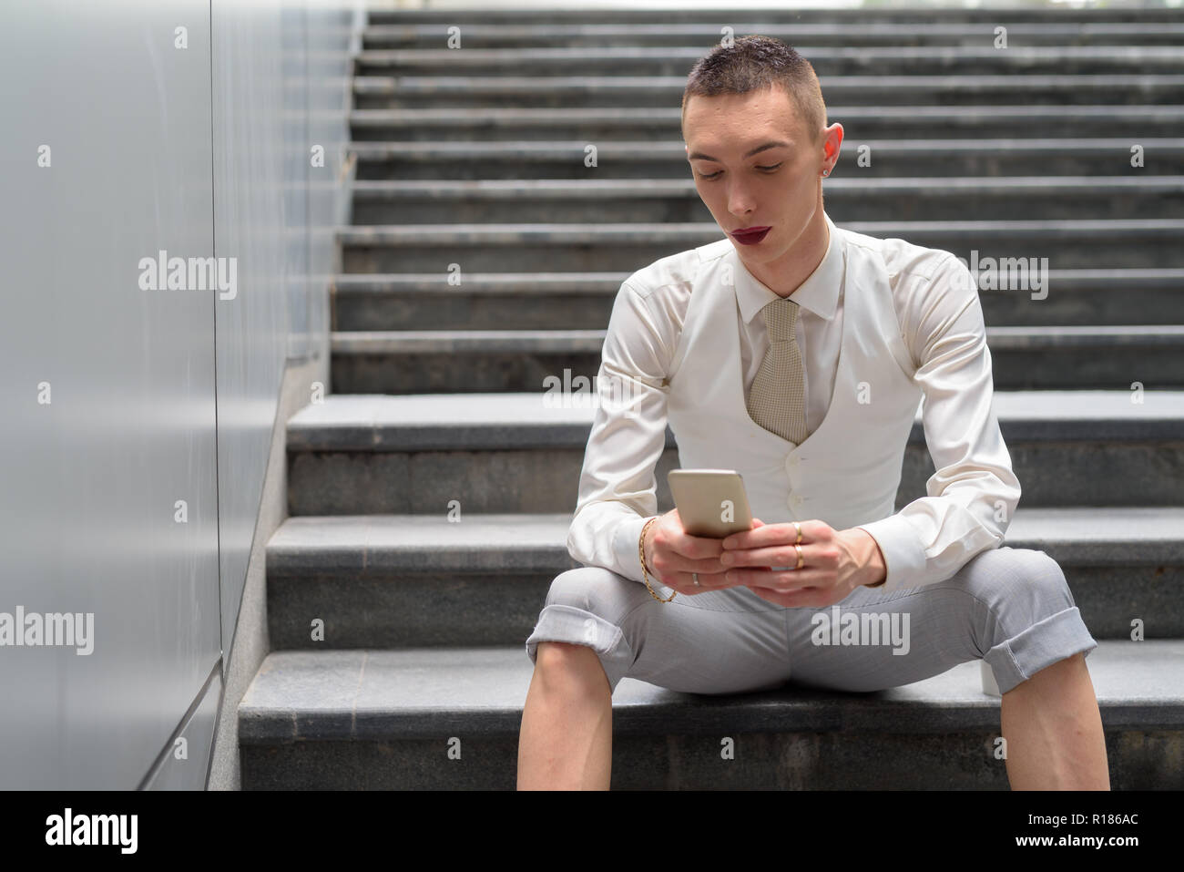 Les jeunes LGBT homosexuel androgyne businessman sitting on stairs lors de l'utilisation de Phone Banque D'Images