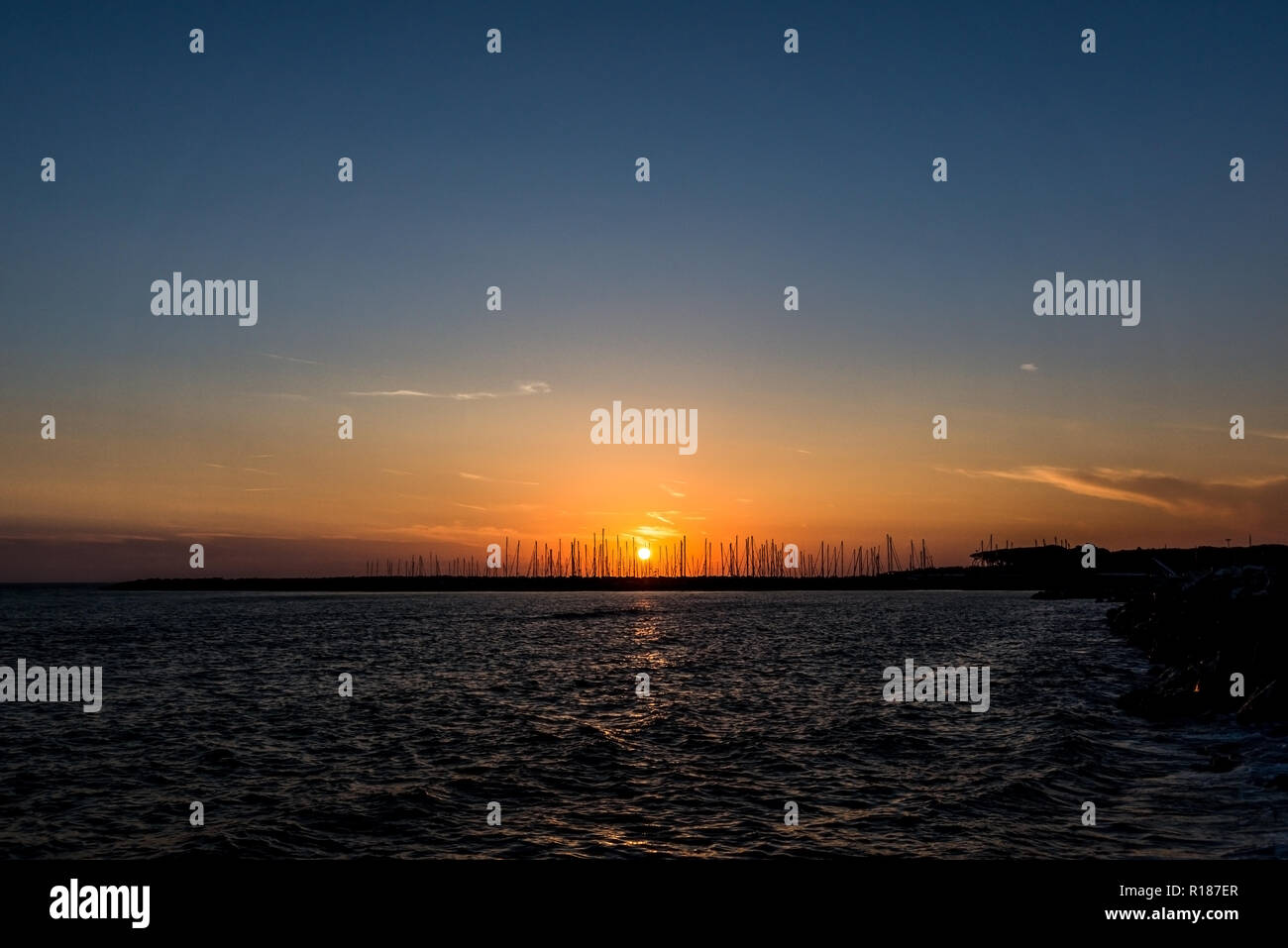 Photo horizontale avec coucher de soleil sur la mer Méditerranée. Soleil est en arrière-plan derrière la jetée en pierre d'ancrage où plusieurs bateaux et navires. Ciel est clair w Banque D'Images