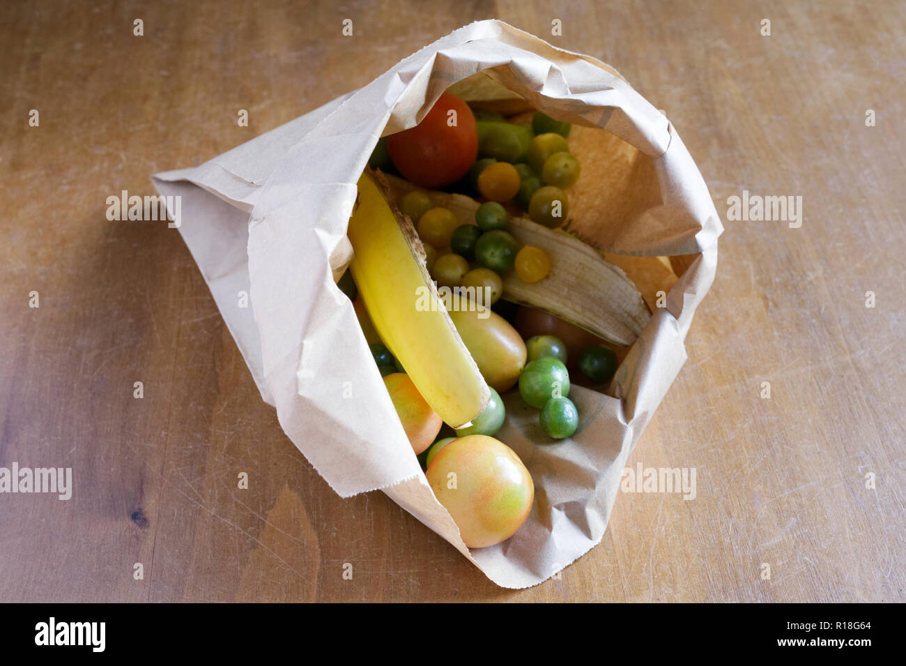 Les tomates vertes de maturation dans un sac en papier brun, avec des peaux de banane. Banque D'Images