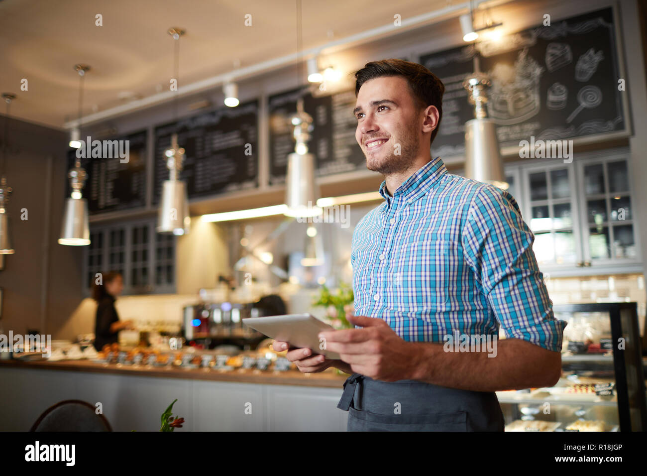 Jeune brunette en workwear standing dans la cafétéria moderne avec contre sur le contexte Banque D'Images