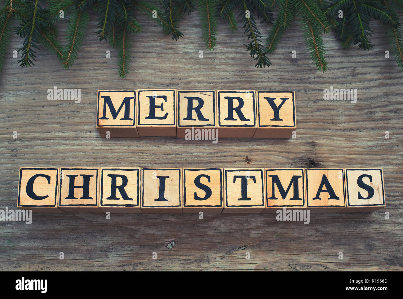 Cubes en bois avec des lettres forme le texte anglais Joyeux Noël. Ils sont couchés sur un fond de bois. Branches de sapin cadre à la photo. Banque D'Images