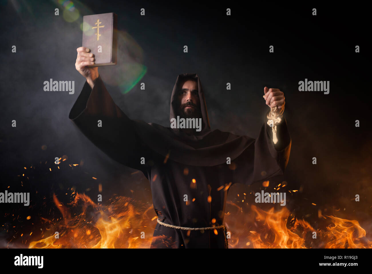 Moine médiéval est en feu avec réserve en mains dans le feu, fond noir, rituel secret. Frère mystérieux dark cape. Mystère et spiritualité Banque D'Images