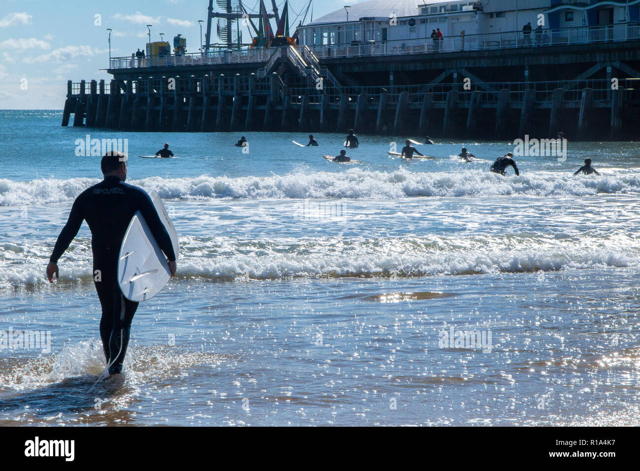 Surfers dans la mer sur la plage de Bournemouth en plein été, en dessous de la célèbre jetée Banque D'Images