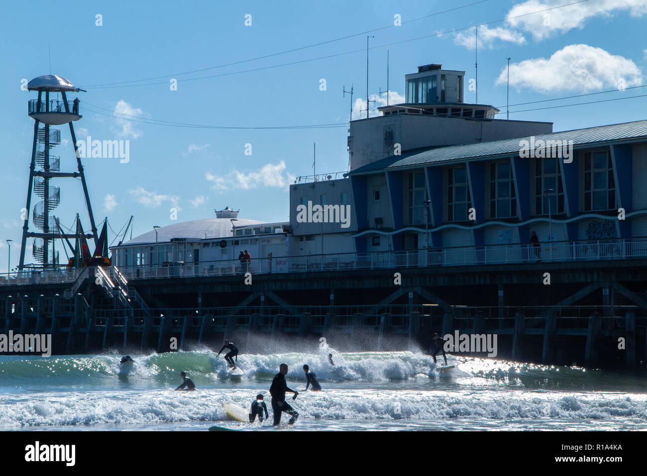 Surfers dans la mer sur la plage de Bournemouth en plein été, en dessous de la célèbre jetée Banque D'Images