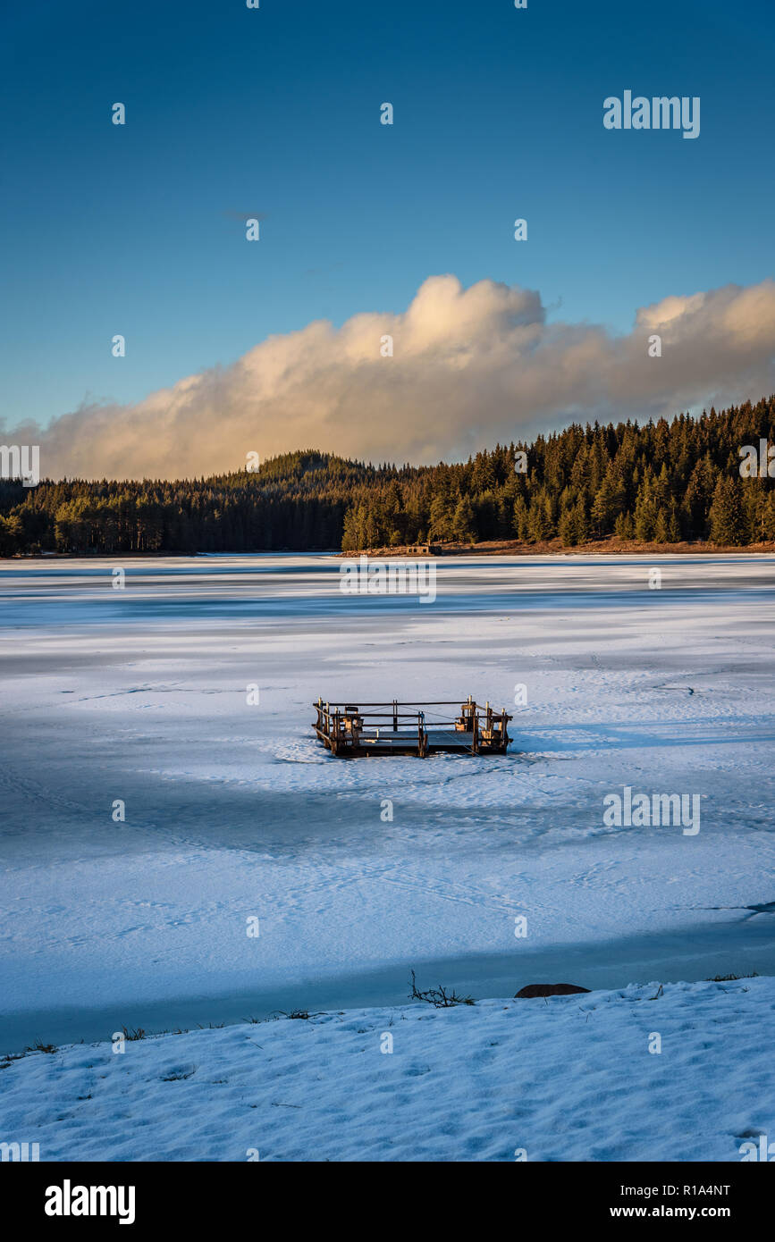 Beau paysage d'hiver sur un lac gelé en montagnes des Rhodopes - coucher de soleil sur la glace fissurée, radeau en bois au milieu de la GI de la pile Banque D'Images