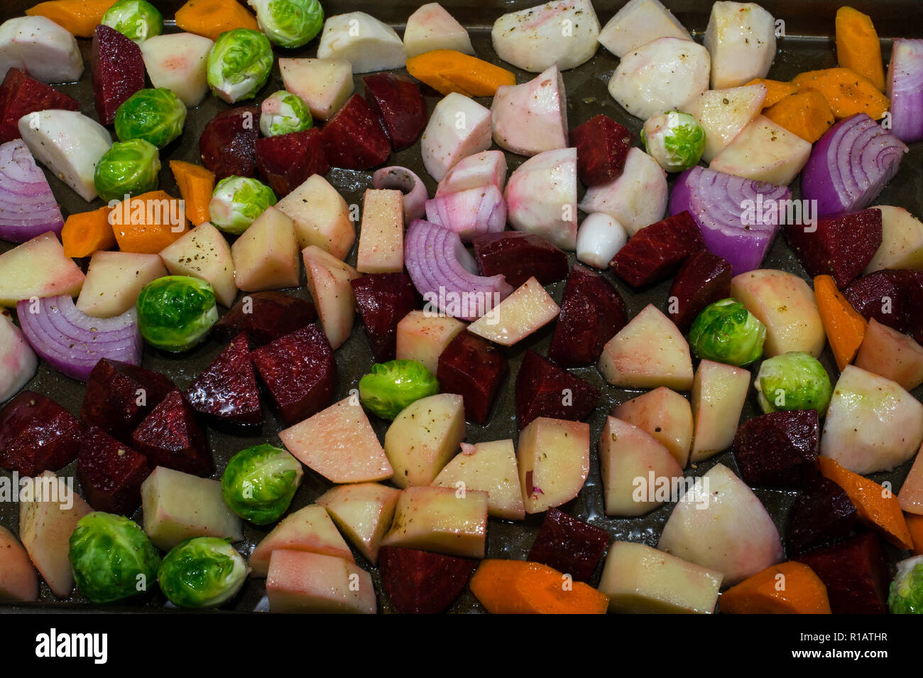 Tranches de légumes d'automne et huilées avant de la faire rôtir. Le medley comprend les pommes de terre, oignons, betteraves, navets, carottes et choux de Bruxelles. Banque D'Images