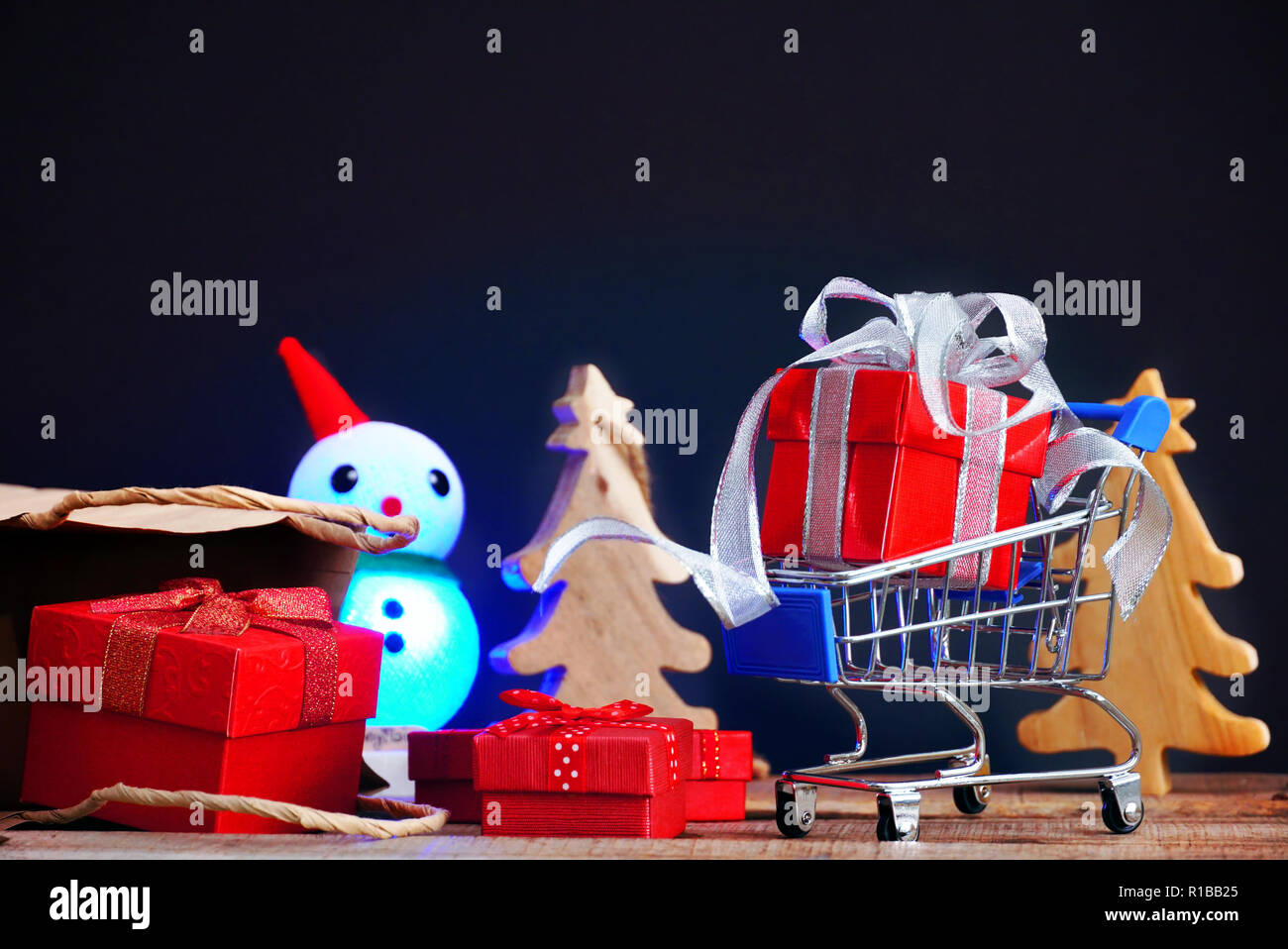 Boîte cadeau rouge sur petit panier avec des boîtes-cadeaux débordent de sac en papier et christmad arbre sur fond noir pour le black friday shopping concept. Banque D'Images