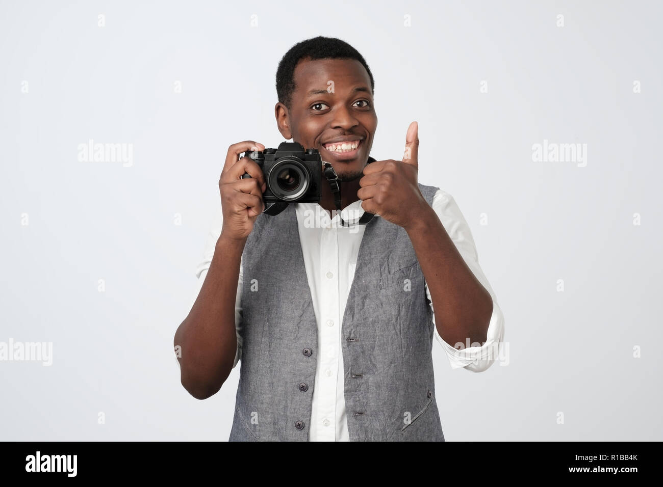 Bel homme africain holding photo appareil photo et souriant, showing thumb up. Hobby concept. Banque D'Images