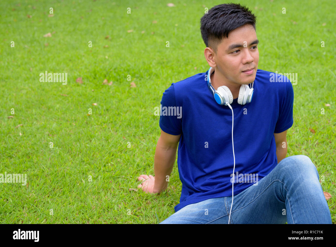 Beau jeune homme asiatique se détendre au parc avec des écouteurs Banque D'Images