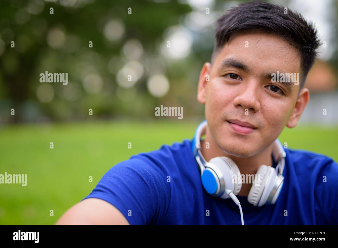 Beau jeune homme asiatique se détendre dans le parc portant des écouteurs Banque D'Images