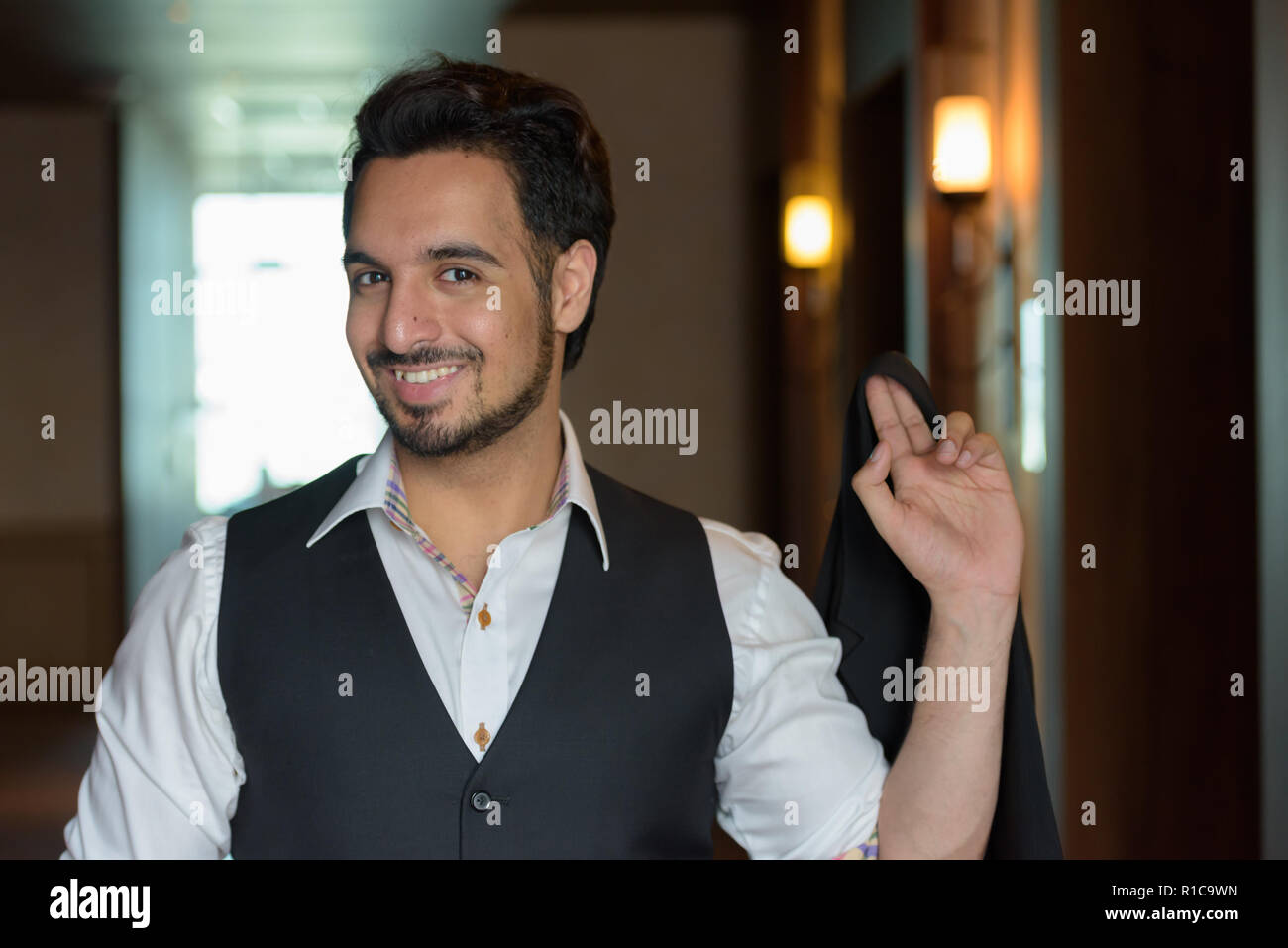 Young happy Indian man smiling while holding veste dans les corri Banque D'Images