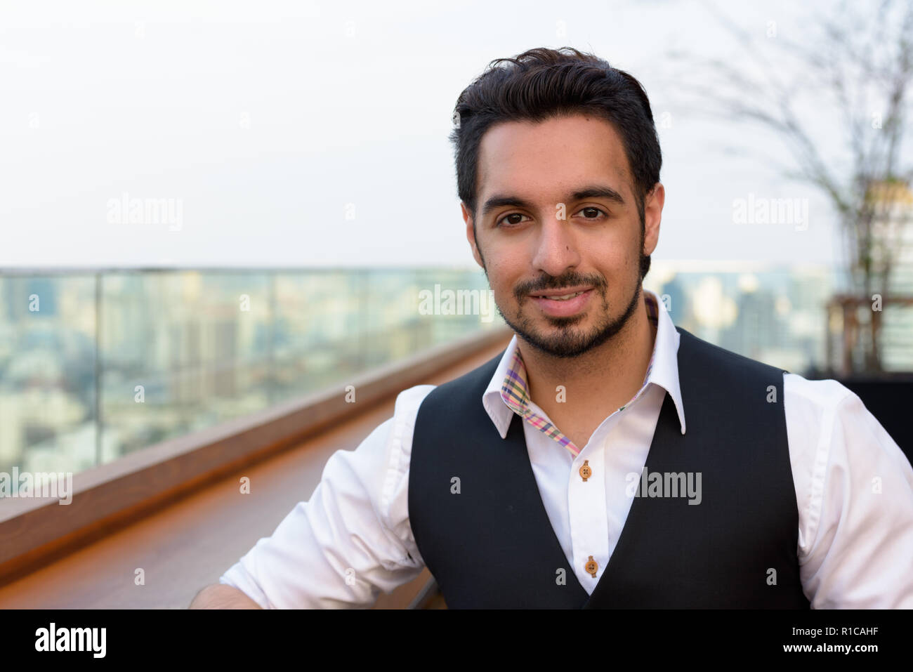 Young happy Indian man smiling at rooftop restaurant à Bangkok Banque D'Images