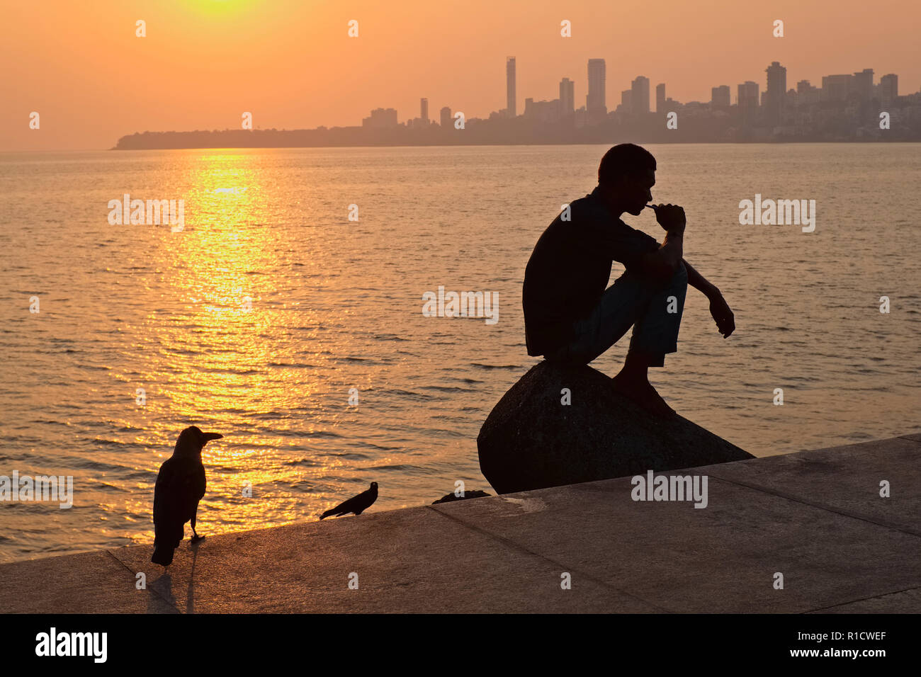 Un homme est assis à Marina Drive, Bombay, la promenade principale de la ville, frappant un penseur entraînent et apparemment vu par deux de ses corbeaux omniprésent Banque D'Images