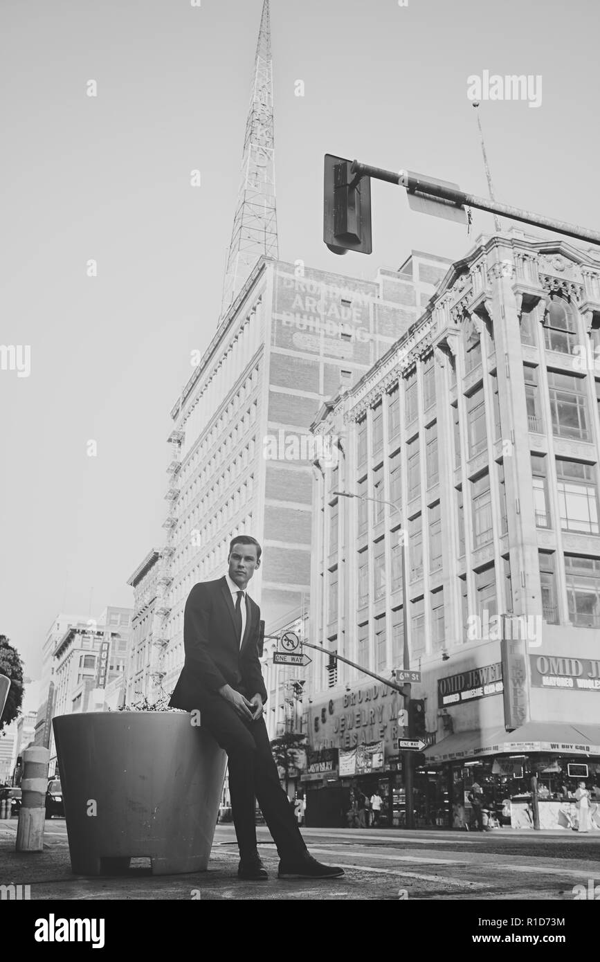 Un portrait en noir et blanc d'un mode d'hommes en costume et cravate assis par les rues de Los Angeles, avec un bâtiment d'époque dans l'arrière-plan. Banque D'Images