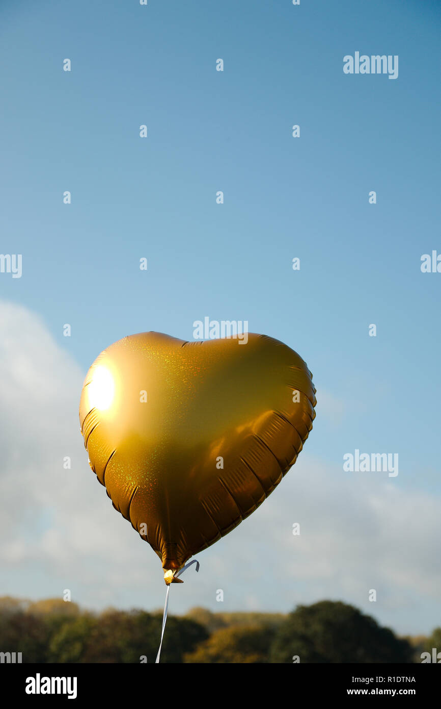 Un ballon en forme de coeur or voler contre un fond de ciel bleu, avec copie espace en mode portrait Banque D'Images